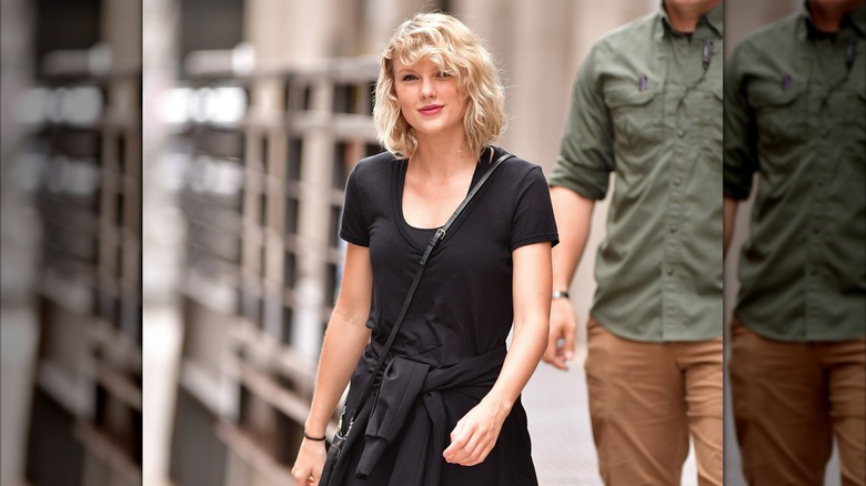 Taylor Swift in an all black outfit with short hair and a small smile.