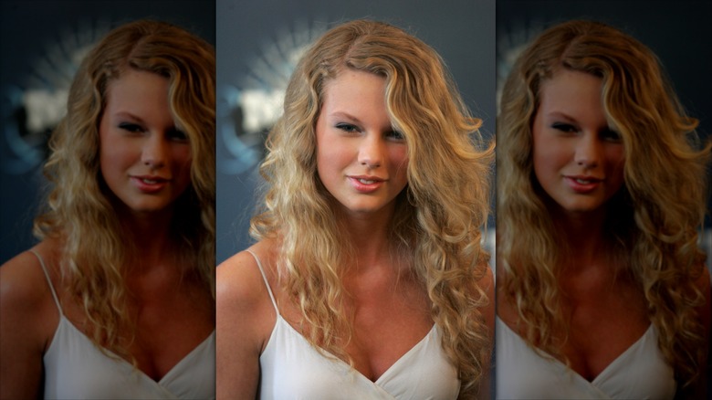 Young Taylor Swift in a white dress in front of a gray background.
