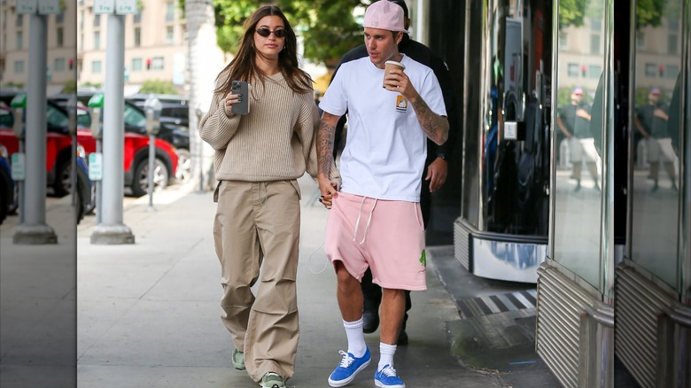Hailey Bieber in all-beige outfit, holding hands with Justin Bieber in white shirt and pink shorts