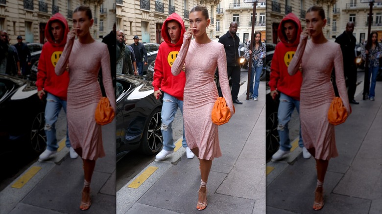 Justin Bieber wearing red sweatshirt and jeans, walking behind Hailey Bieber in pink dress