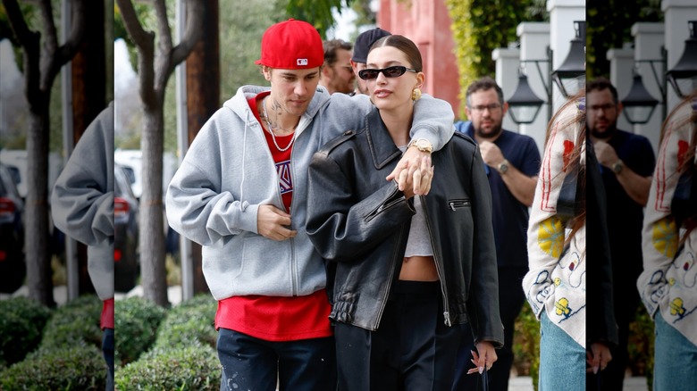 Justin Bieber wearing jeans and a sweatshirt with arm around Hailey Bieber in a leather jacket