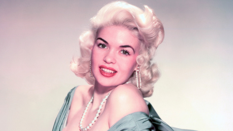 Jayne Mansfield wears a green dress, pearl necklace, and elongated hoop earrings.