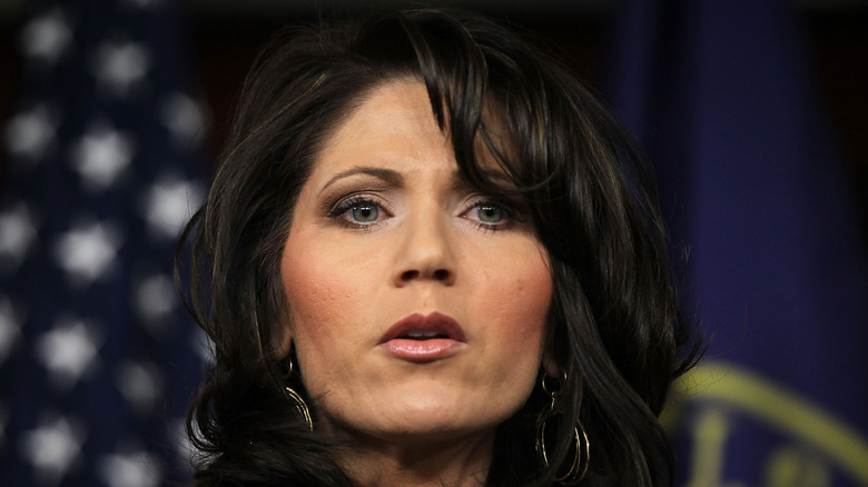 Kristi Noem speaking at a news conference while wearing a black blazer.
