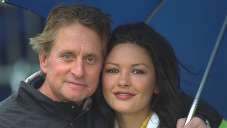 Michael Douglas with his arm around fiance Catherine Zeta-Jones under an umbrella