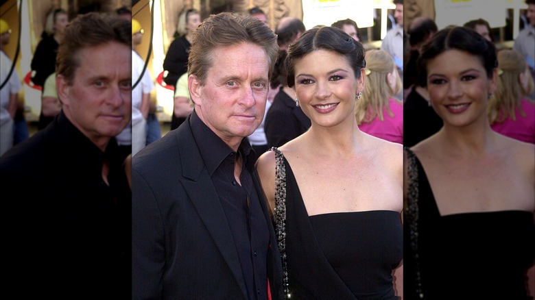 Michael Douglas in an all-black suit with Catherine Zeta-Jones in a black dress on a red carpet.