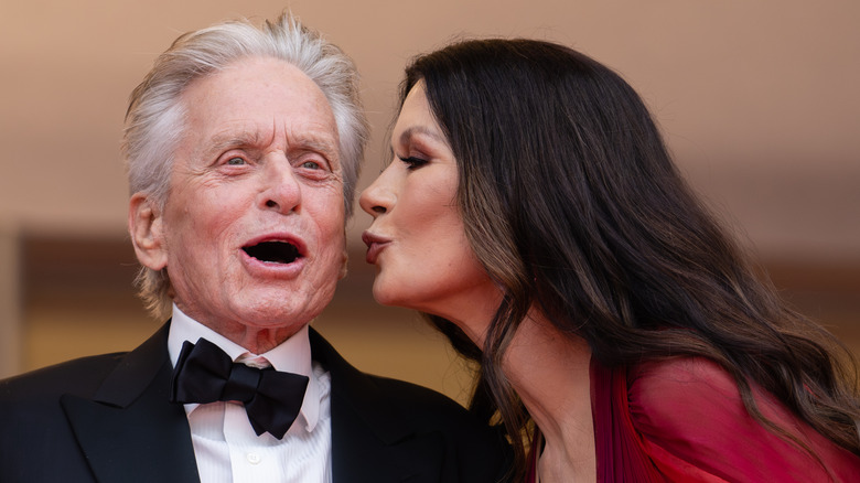 Michael Douglas in a tux with his mouth open and Catherine Zeta-Jones leaning in to kisshis cheek.