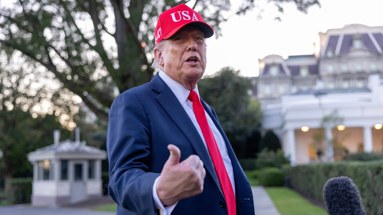 Donald Trump gesturing with his thumb while talking outside the White House.