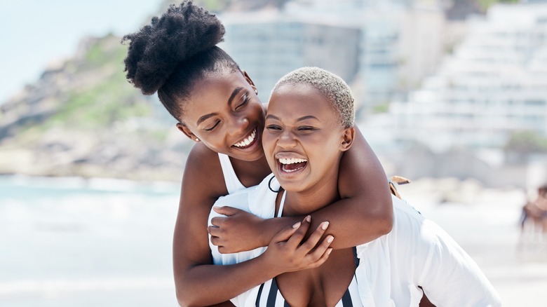 female couple laughing on beach embracing
