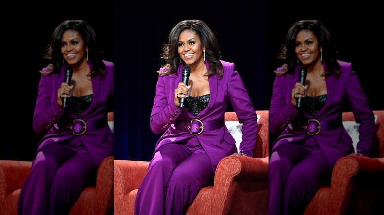 Michelle Obama sitting on stage holding mic wearing purple pant suit