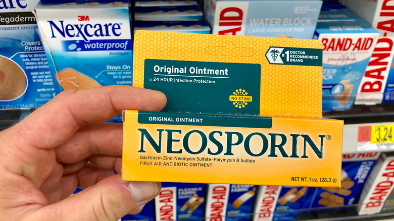 Man holding Neosporin in front of a shelf filled with bandages.