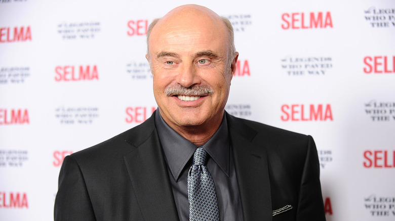Dr Phil smiling at the cameras at the 'Selma' Gala in a black suit with a grey dress shirt and tie
