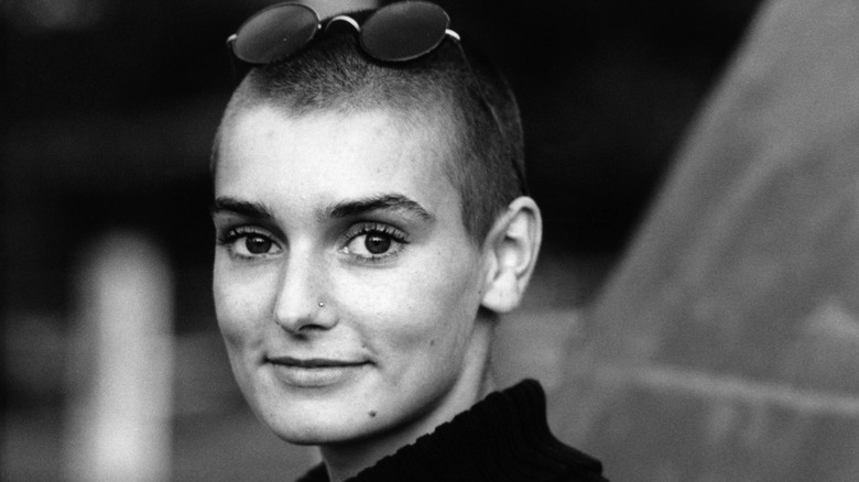 Sinéad O'Connor poses for a black and white portrait with small, circular sunglasses in a black turtleneck