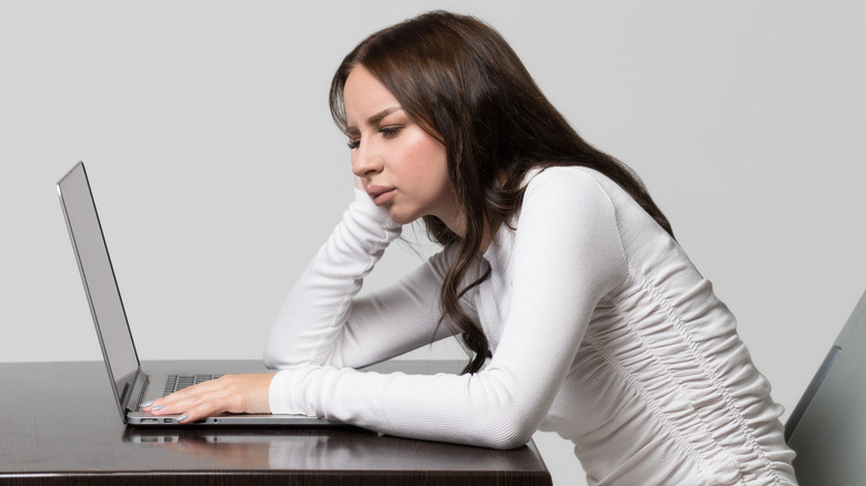 A woman leaning on her elbow over her laptop, demonstrating a posture mistake