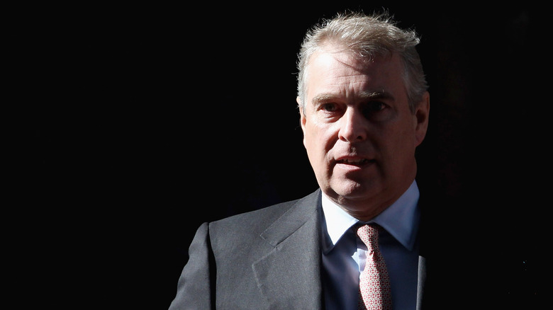 Prince Andrew walking outside against black background with half his face in a shadow
