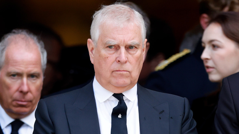 A closeup of Prince Andrew looking grumpy in a black suit