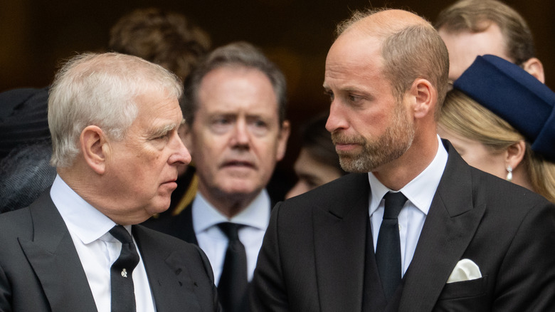 Prince Andrew and Prince William looking at each other while wearing black suits