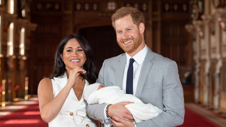 Prince Harry, Duke of Sussex, smiling and holding Prince Archie next to Meghan Markle, Duchess of Sussex