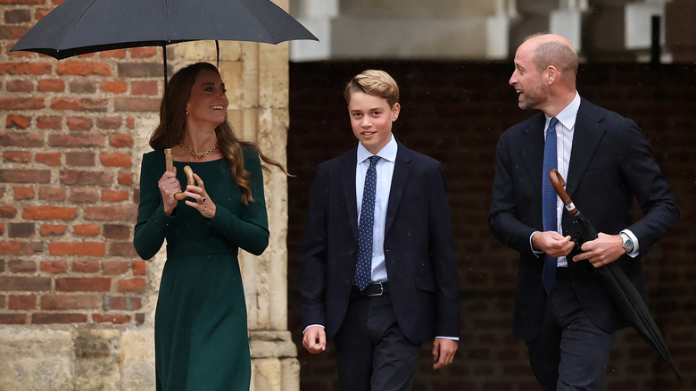 A smiling Prince George walking between Princess Catherine and Prince William on his first day at Eton