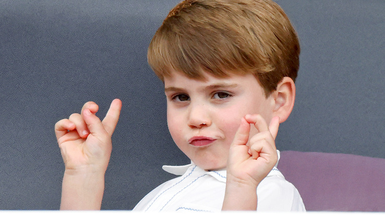Prince Louis smiling mischievously as he points his fingers to the sky