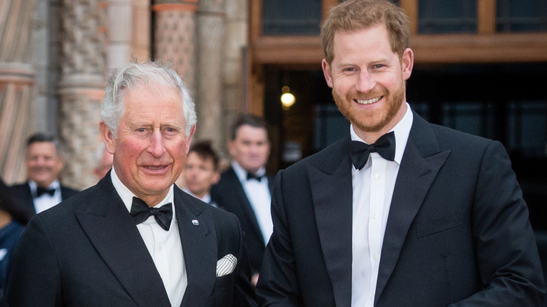 King Charles III and Prince Harry smiling at the camera while posing together in tuxedos