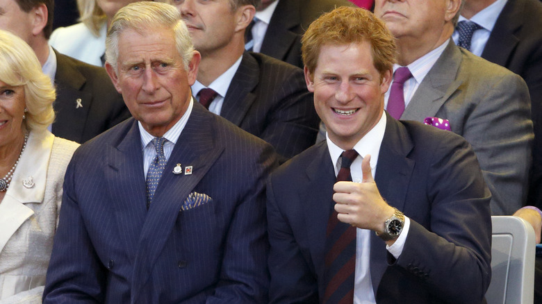 King Charles III seated next to Prince Harry, who is smiling and giving a thumbs up