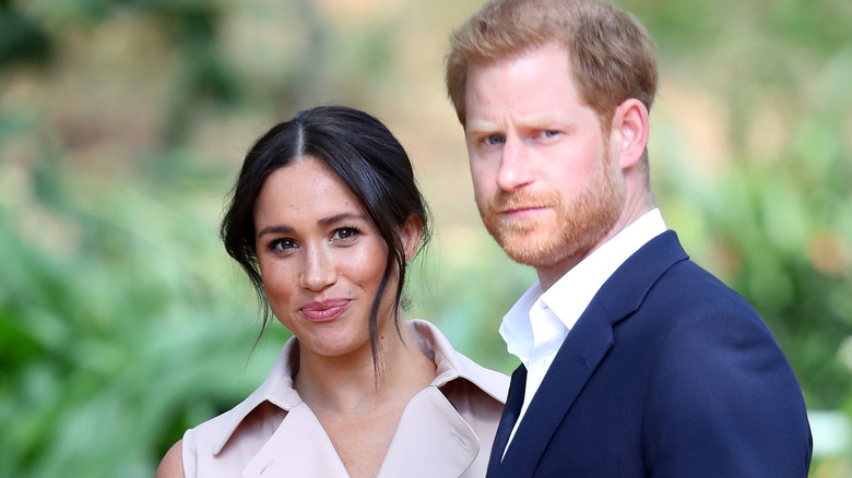 A smiling Meghan Markle standing next to a serious-looking Prince Harry