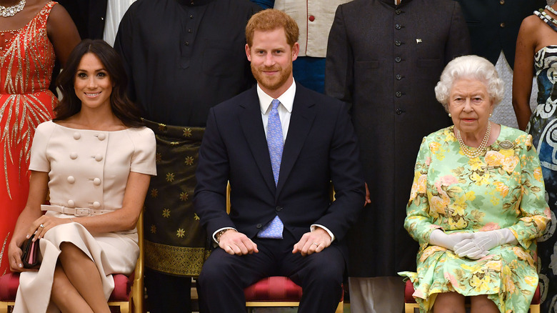 Prince Harry sitting between Meghan Markle and a grumpy Queen Elizabeth II