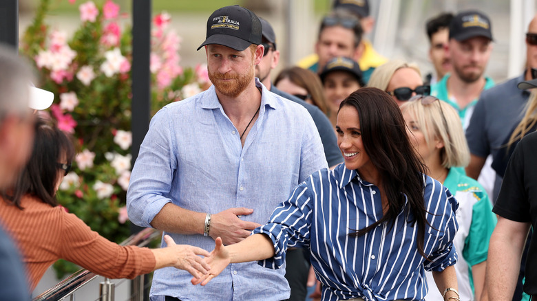 Meghan Markle, Duchess of Sussex, shaking someone's hand in front of Prince Harry, Duke of Sussex
