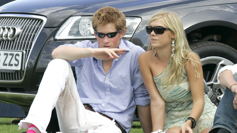 Older photo of Prince Harry and ex girlfriend Chelsy Davy sitting on the grass in front of a car in sunglasses
