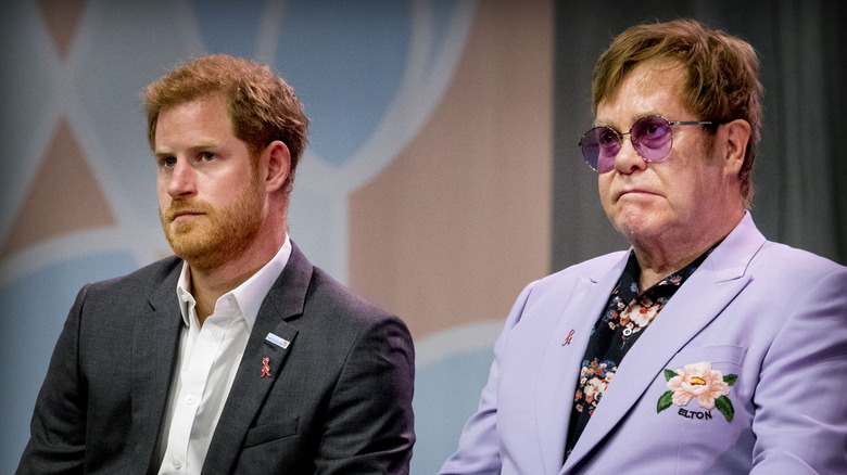 Prince Harry black suit next to Elton John purple and floral suit