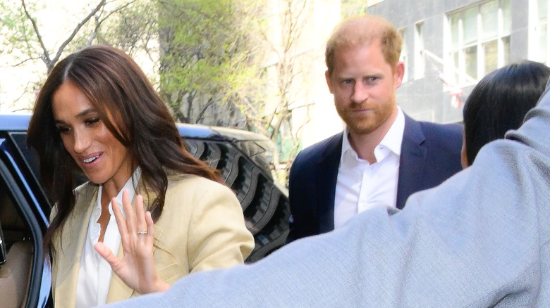 Prince Harry looking surly behind Meghan Markle while entering car