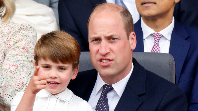 Prince Louis points while seated in the lap of a frowning Prince William.