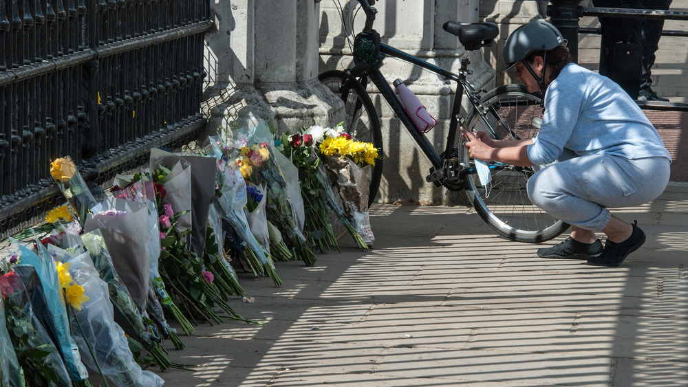 Woman taking photo of flowers left outside gate