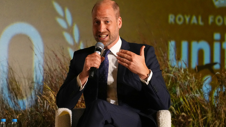 Prince William sitting in a chair in a blue suit and tie