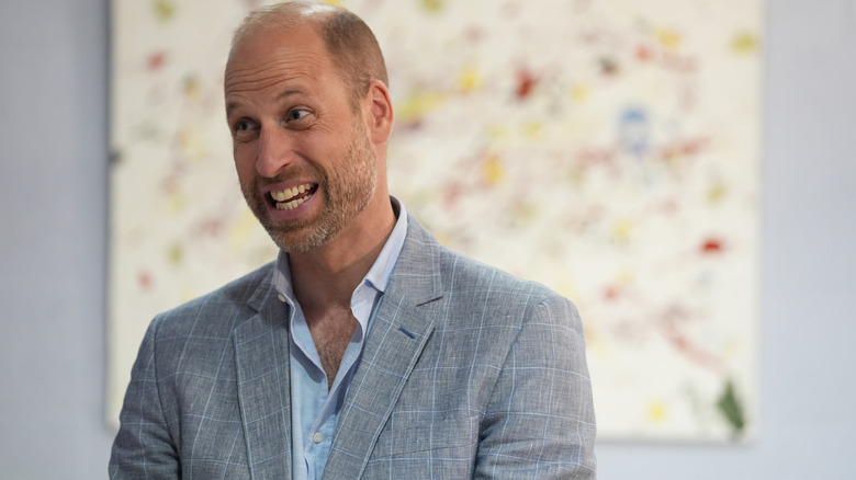 Prince William raisin his eyebrows as he smiles at someone in a grey suit