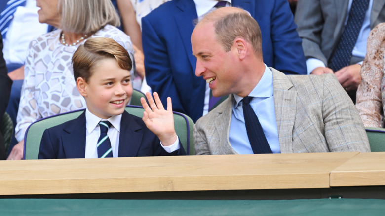 A smiling Prince William speaking to a smiling Prince George