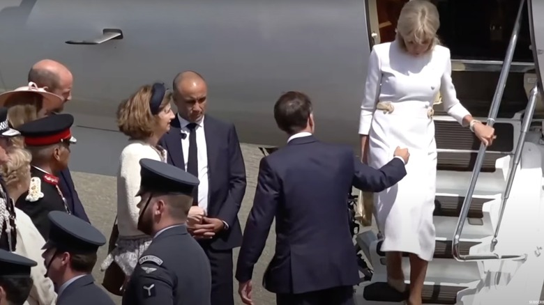 Emmanuel Macron holding his hand out to Brigitte Macron as she walks down the stairs of a plane