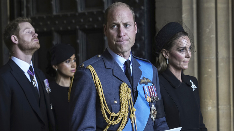 Prince William and Princess Catherine pursing their lips while a concerned-looking Prince Harry and Meghan Markle stand behind them