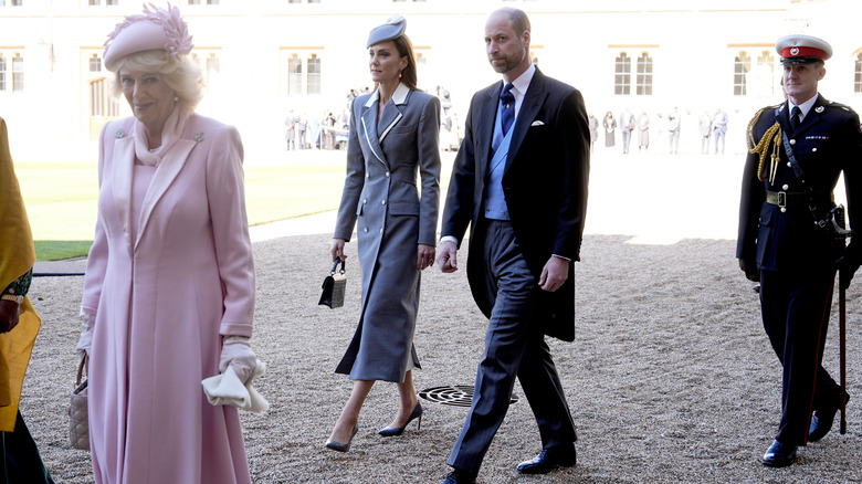 Queen Camilla smiling while William, Prince of Wales looks skeptical and walks beside Catherine, Princess of Wales