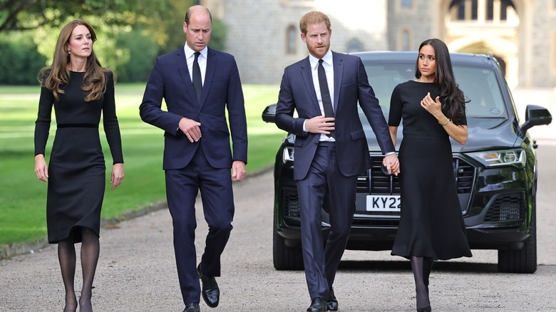 Prince William, Kate Middleton, Prince Harry, and Meghan Markle walking together looking solemn