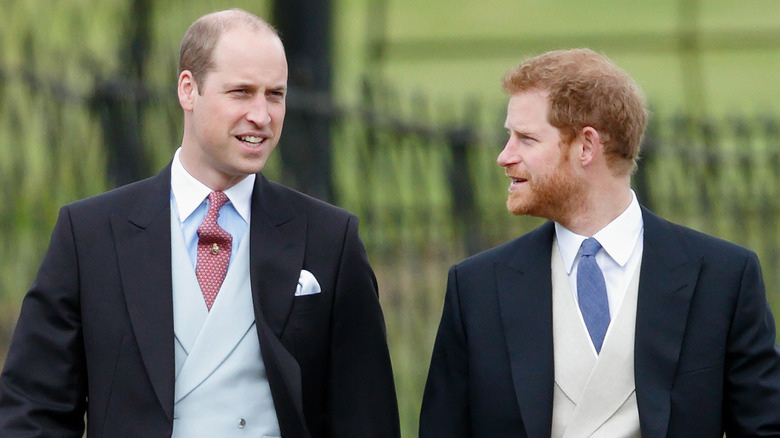Prince William and Prince Harry looking at each other while walking together in black suits