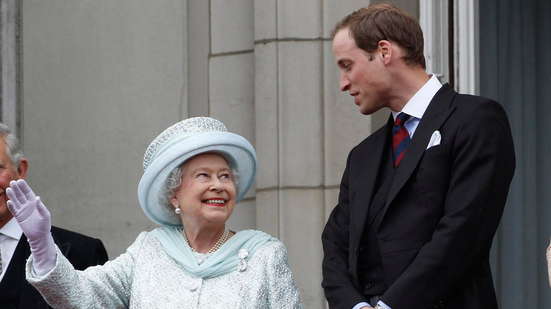 Prince William looking down at Queen Elizabeth II while she waves with a smile.