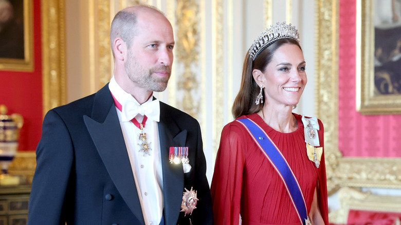Kate Middleton smiling in a tiara and sash next to her husband, Prince William, in a suit with military medals