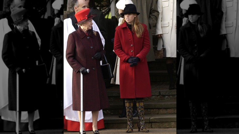 Princess Beatrice wearing bejeweled boots and a red coat while standing beside Queen Elizabeth II.