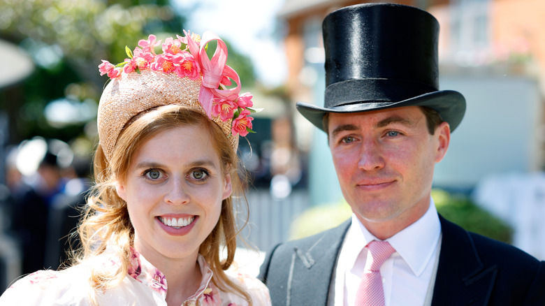 Princess Beatrice wearing a pink dress and a hat smiling next to Edoardo Mapelli Mozzi who's wearing a suit and hat.