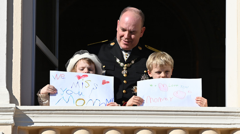 Prince Albert with his children Princess Gabriella and Prince Jacques holding up signs for Princess Charlene