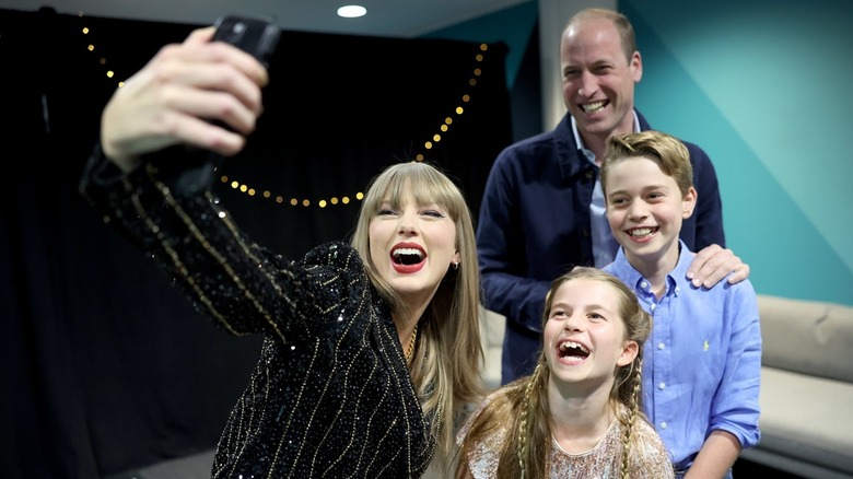 Taylor Swift smiling and taking a selfie with Princess Charlotte, Prince George, and Prince William