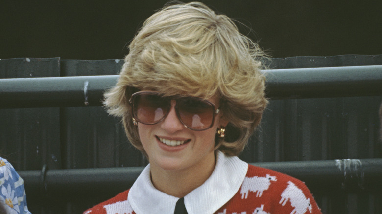 Princess Diana smiling while wearing sunglasses in her famous sheep sweater