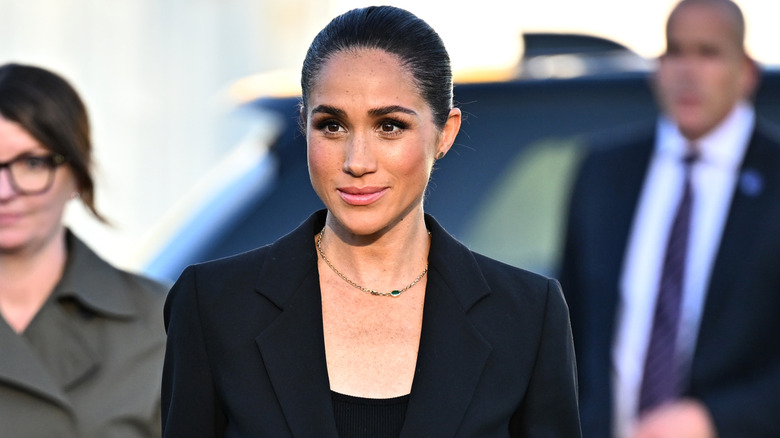 Meghan Markle smiling in a black suit with her hair in a slicked-back bun