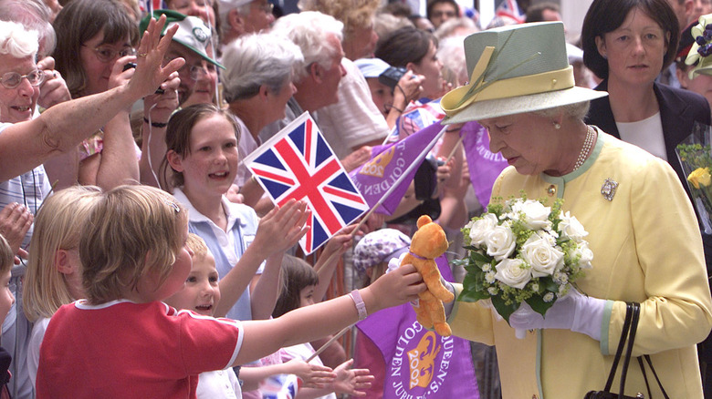 Queen Elizabeth II receiving a teddy bear from a child in an all-yellow outfit